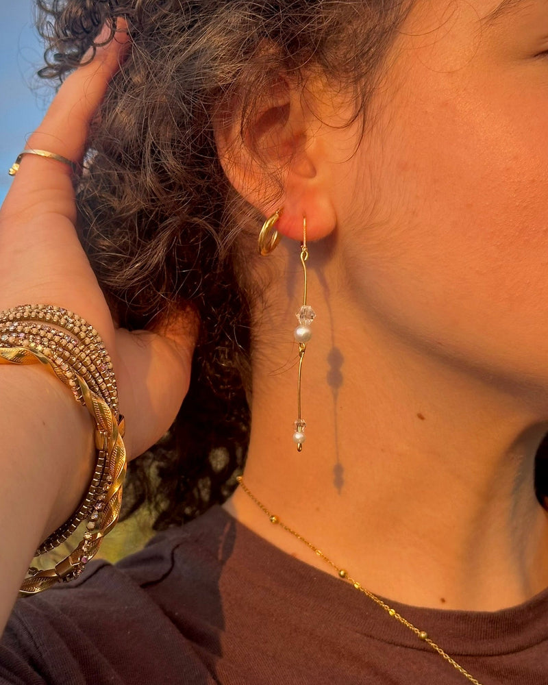 Close-up of a person wearing gold earrings and bracelets against a blue sky.